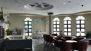 A spacious room with a high ceiling, large arched windows, and a central seating area with chairs and a table.