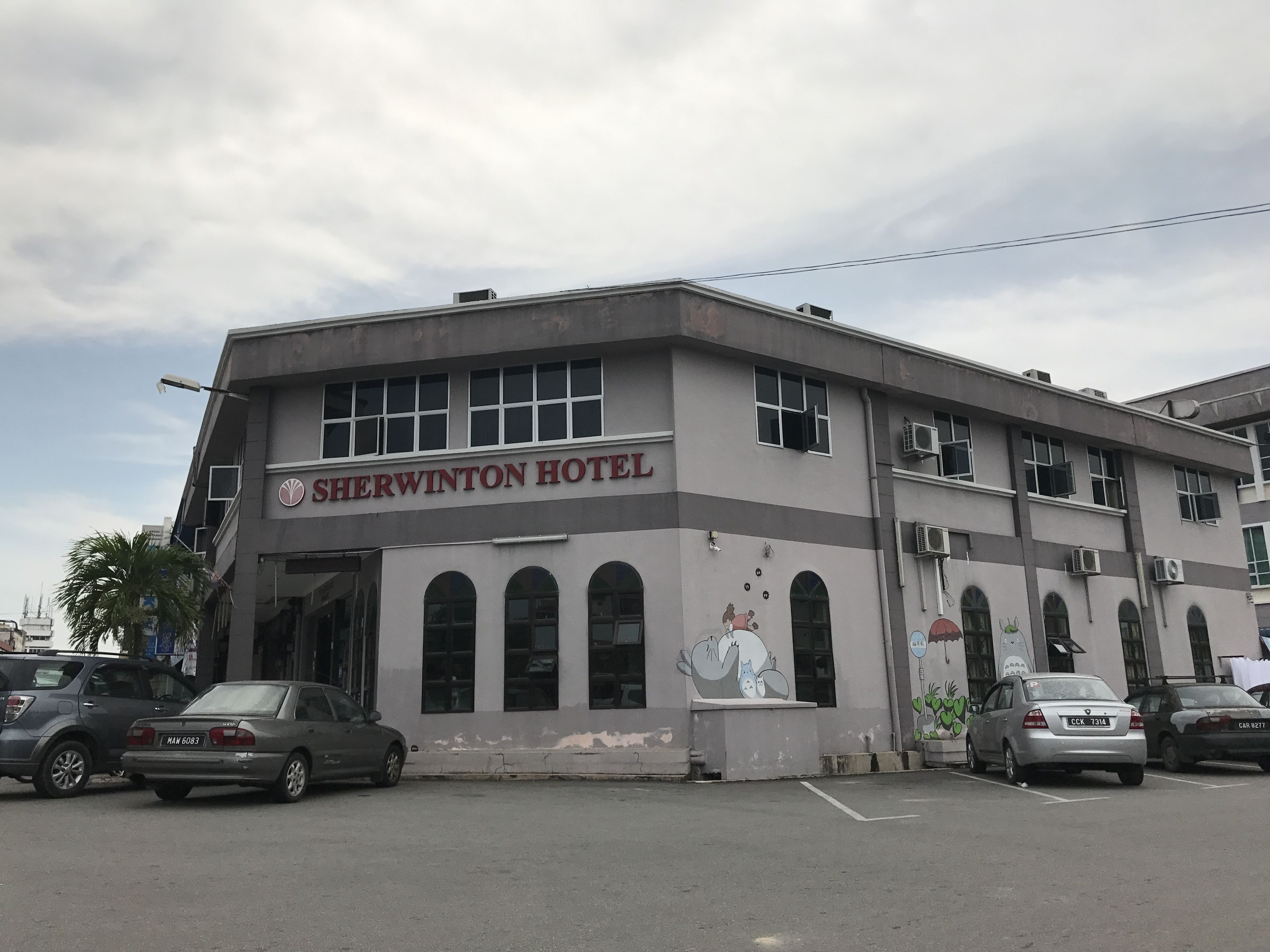 A Sherwinton Hotel with a simple facade, multiple windows, and a parking lot with several cars.
