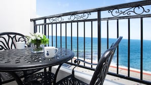 Una mesa metálica redonda con sillas, una planta en maceta y una taza blanca en un balcón con vistas al mar.