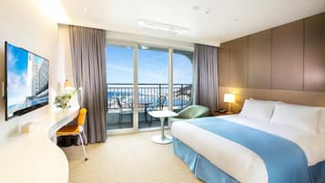 Habitación de hotel con una cama grande, un escritorio con una silla, una mesita y un balcón con vista a la ciudad.