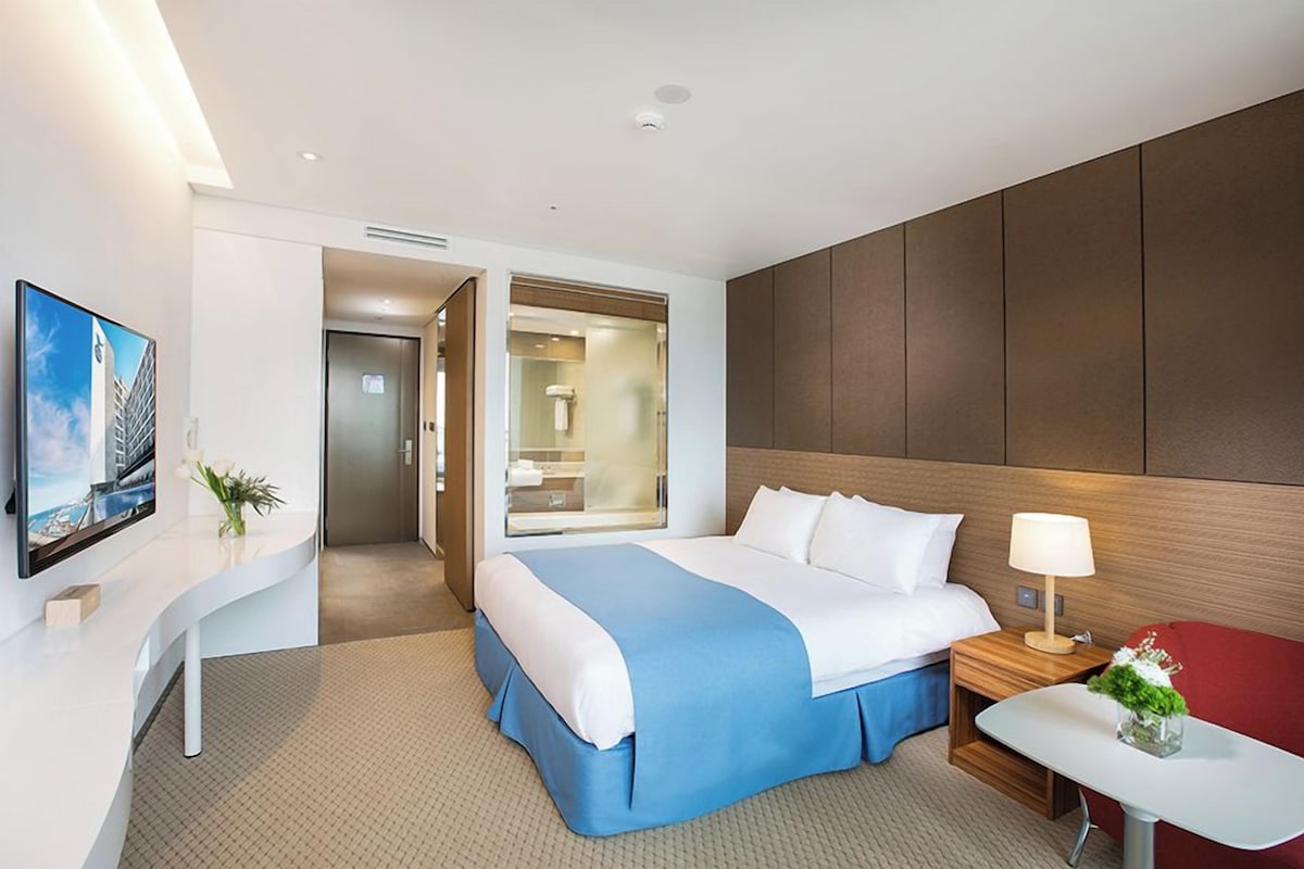 Habitación de hotel moderna con cama, mesita de noche, lámpara y vistas a la ciudad.