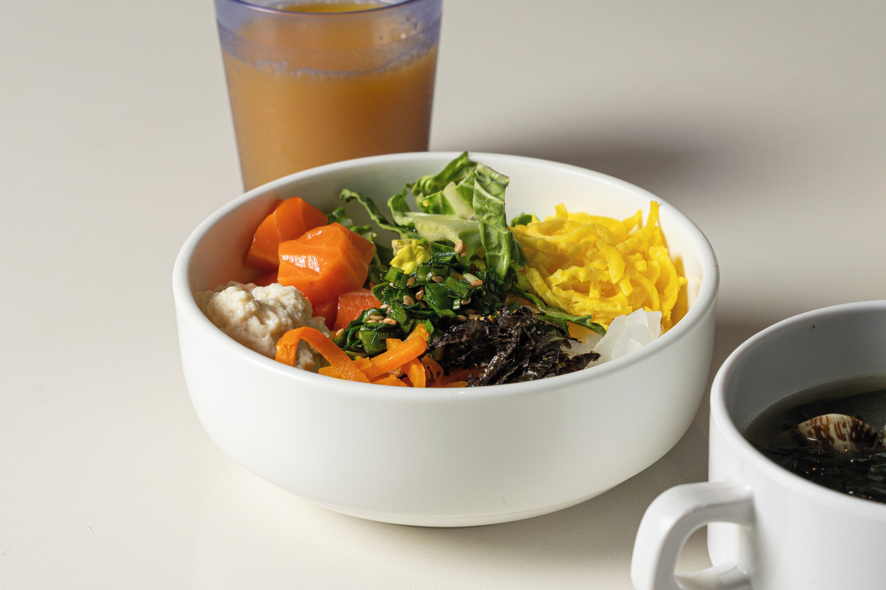 A bowl of food with vegetables and a cup of tea.