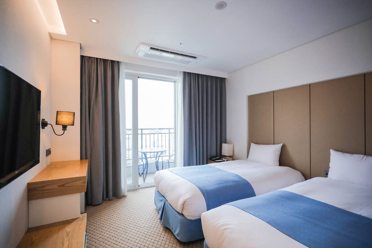 A hotel room with two beds, a TV, a desk, and a balcony with a table and chairs.