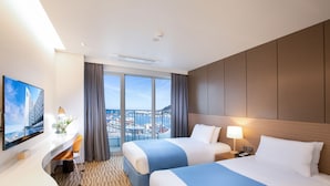 Habitación de hotel con dos camas, un escritorio, un televisor de pantalla plana, vistas a la ciudad a través de ventanas amplias y un balcón.