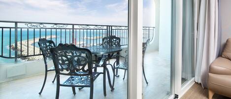 A balcony with a table and chairs, overlooking a beach and the ocean.