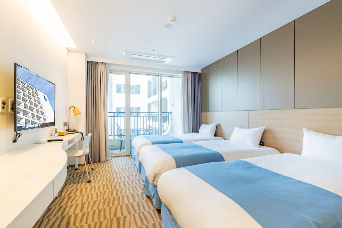 A hotel room with two beds, a desk, a chair, a TV, and a balcony with curtains.