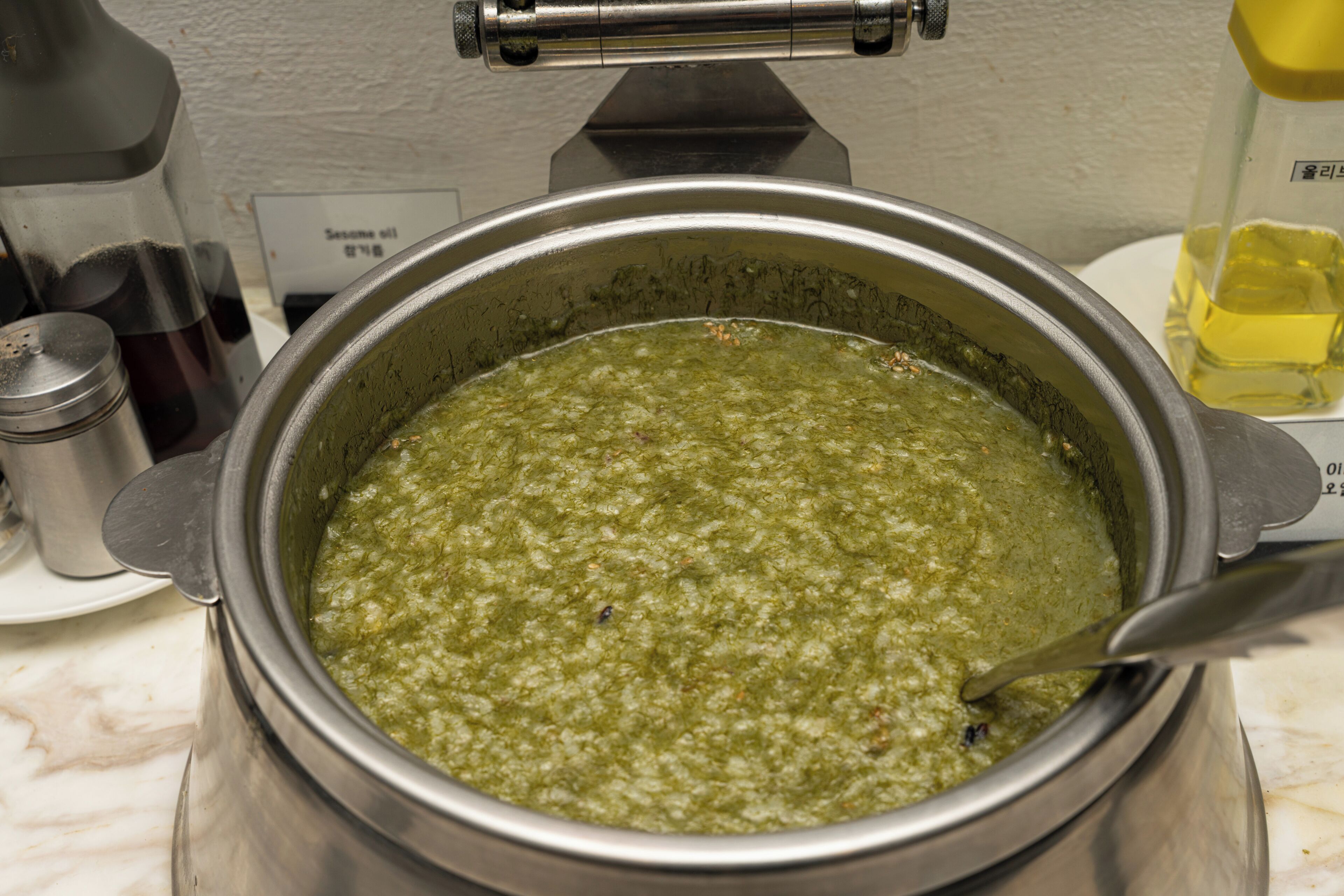 A stainless steel pot with a green mixture, a metal container with a black lid, and a bottle with a yellow cap.