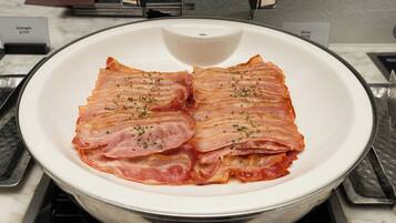 A white plate with bacon strips on a kitchen counter.