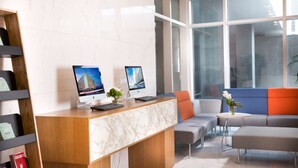 Un mostrador de recepción con dos monitores, una planta y una zona de estar con sofá y reposapiés.