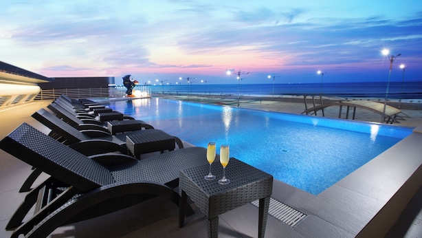 Zona junto a la piscina con sillones de descanso y una mesa con dos copas de champán, con vistas al mar.