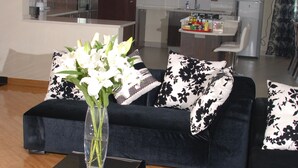 A modern living room with a black sofa, a coffee table with a vase of white flowers, and a black and white rug.