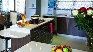A modern kitchen with a dining area, featuring a central island, dark cabinetry, and a large window with patterned curtains.