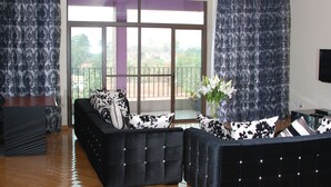 A living room with a black sofa, a small side table, and a large window with a view of buildings and trees.