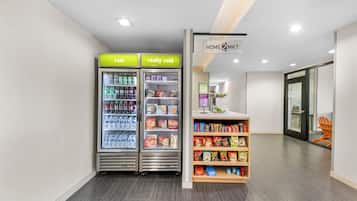 Interior limpo e moderno, com dois dispensadores de bebidas identificados como 'frio' e 'bem frio', e uma prateleira de petiscos repleta de diversos produtos.