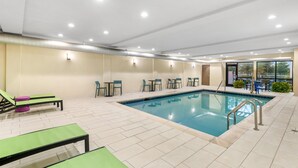 Piscina interior con sillones de descanso, mesas y sillas, rodeada por un suelo de baldosas y paredes con iluminación empotrada.