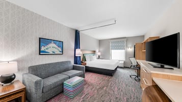 Una habitación de hotel con cama, sofá, televisor, escritorio y piso alfombrado.