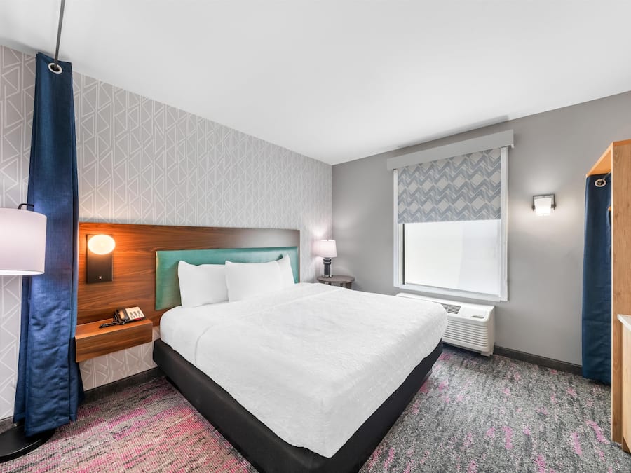 A hotel room with a bed, a nightstand, a lamp, a window, and a wardrobe.