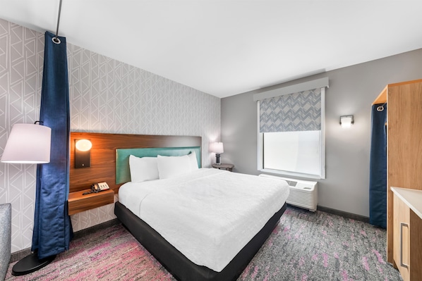 Une chambre d’hôtel comprenant un lit, une table de chevet, une lampe, une fenêtre et une armoire.