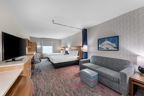 Una habitación de hotel con cama, sofá, televisor, escritorio y un ventanal grande.