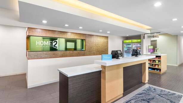 Zona de recepción de hotel con diseño moderno, una mesa de recepción, un minibar y un quiosco digital.