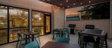 An outdoor patio with tables and chairs, a stone wall, and a view of a building with a baseball field.