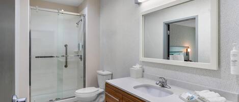A modern bathroom with a glass-enclosed shower, a white toilet, a vanity with a mirror, and a sink.