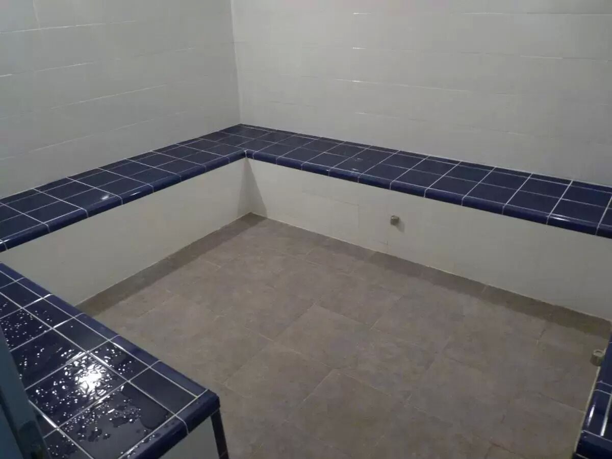 A small bathroom with blue-tiled walls and floor, a white toilet, and a small sink.