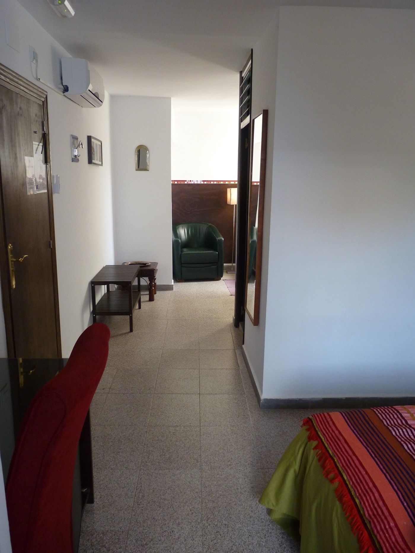 A hotel room with a bed, a red chair, a wooden table, and a green armchair.