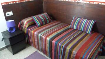 Une chambre avec une tête de lit en bois, deux lits avec une literie à rayures, une table de chevet avec une lampe et un tapis violet.