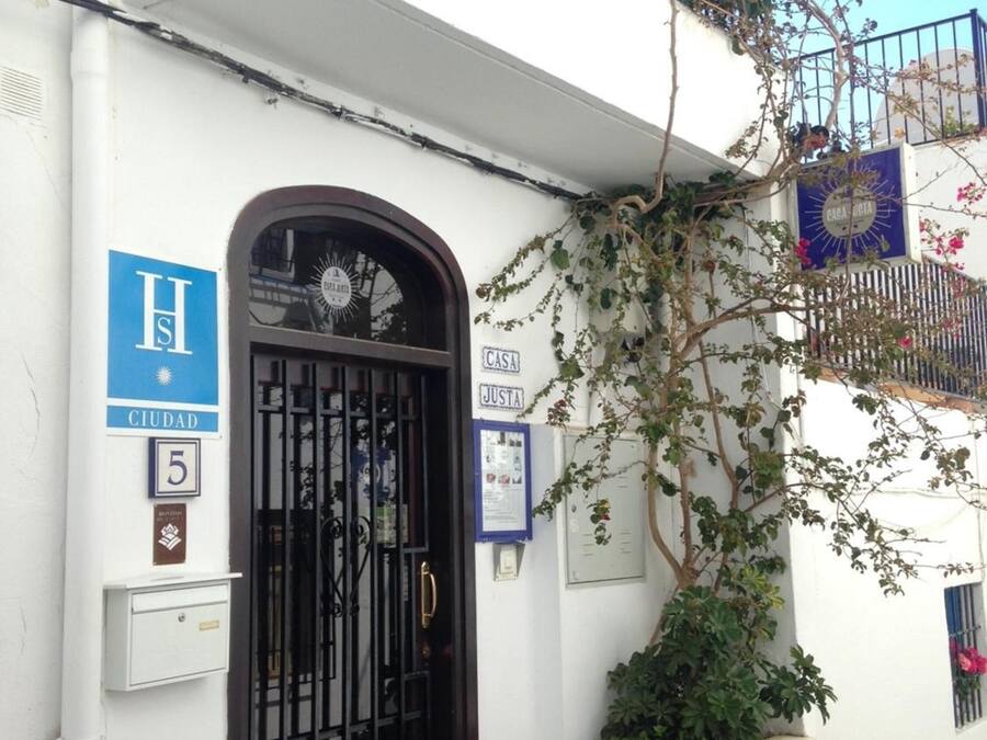 Un edificio blanco con un portón negro, un letrero azul que dice 'H' y 'CIUDAD', y un letrero con el número '5'.
