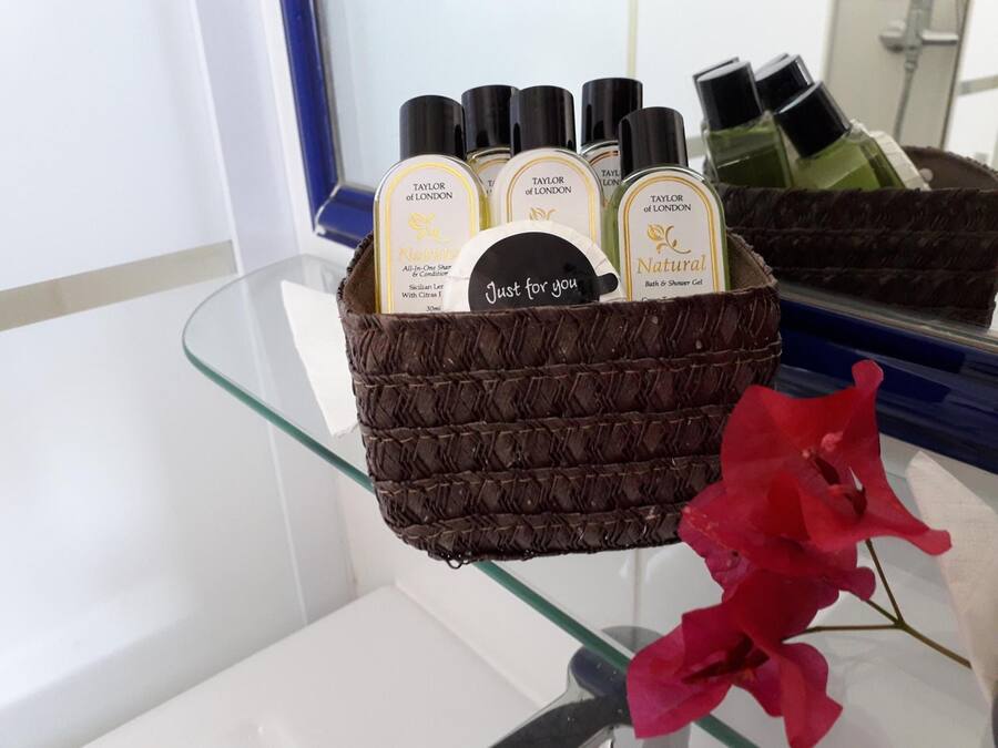 A bathroom shelf with a basket containing several bottles of Taylor of London bath and shower gel, a card with the text "Just for you," and a red flower.