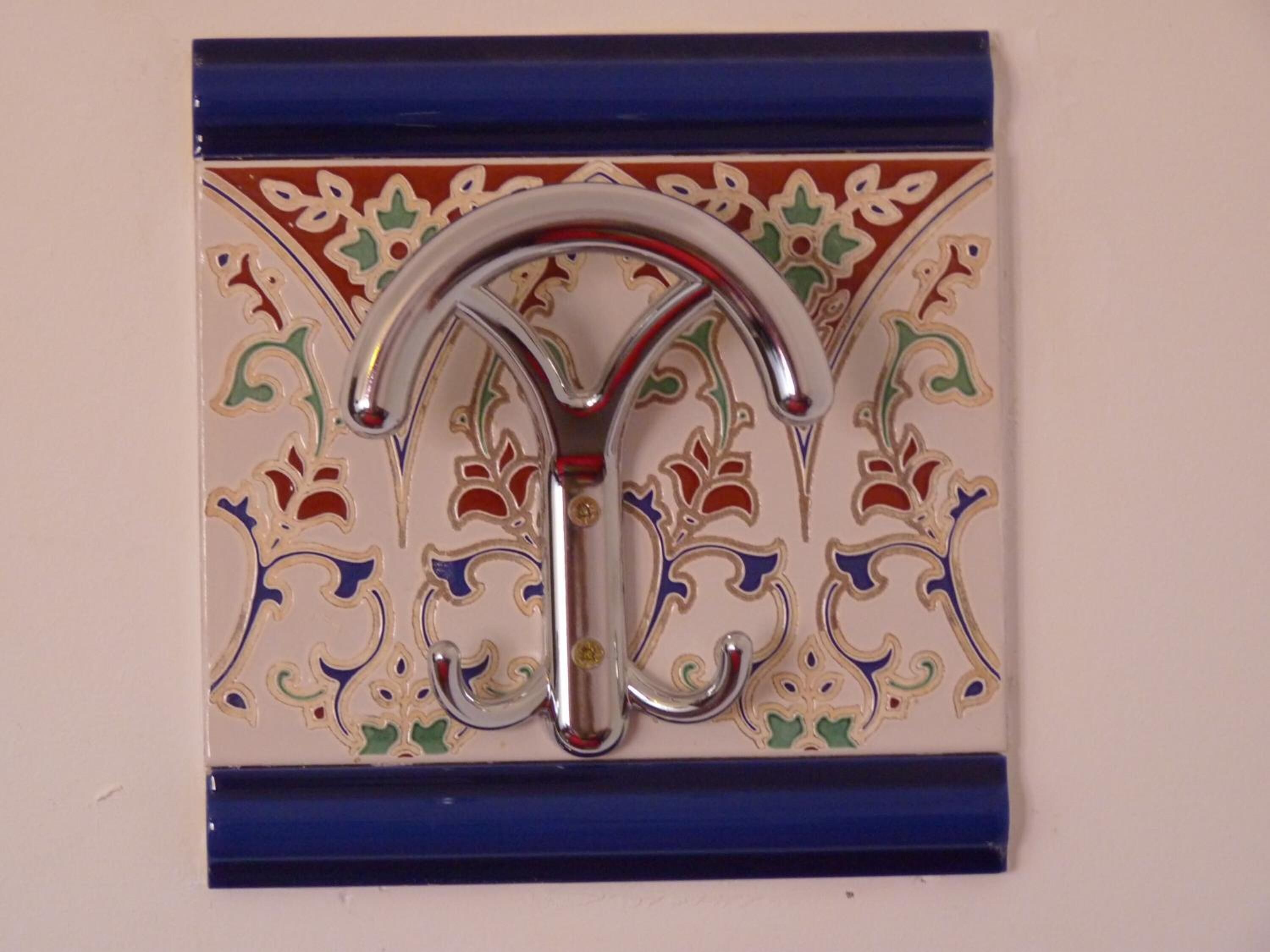 A decorative metal object with a curved handle, mounted on a wall with ornate tile patterns.