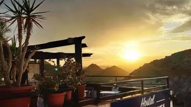 Un cartel que dice 'Hostal CASA JUSTA' con vista a la puesta de sol y montañas al fondo.