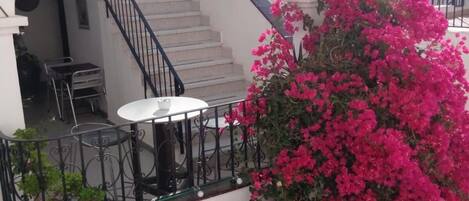 A hotel with a staircase, outdoor seating, and a balcony with pink flowers.