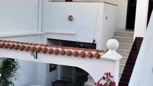 Un edificio blanco con techo de tejas, un balcón y una escalera que lleva a un nivel superior.