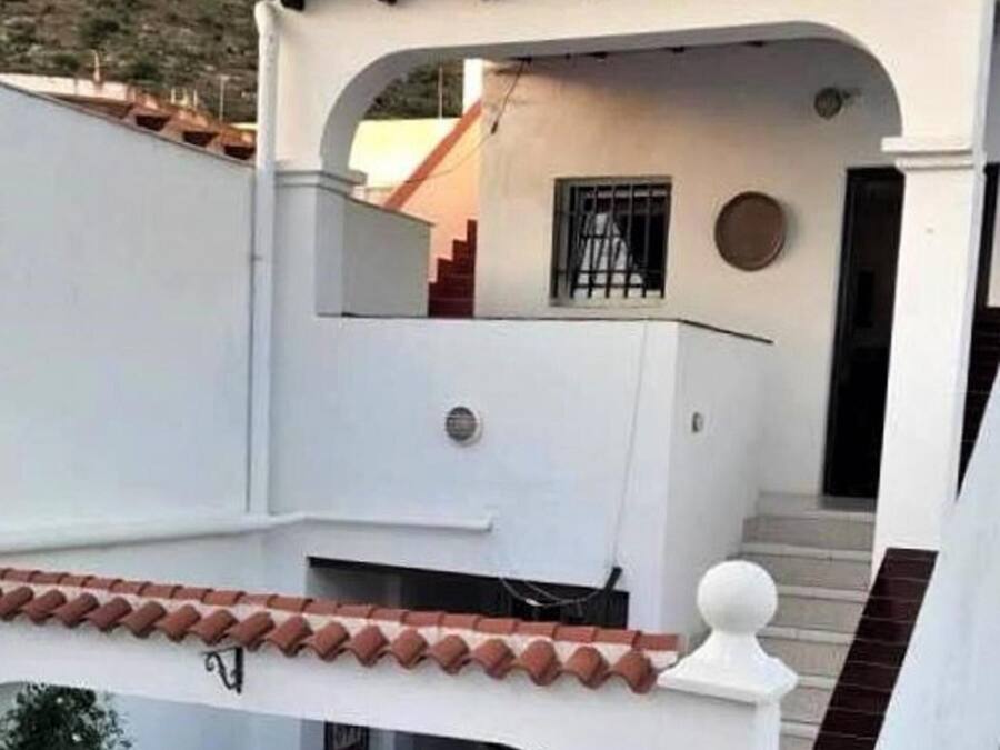 A white building with a tiled roof, a balcony, and a staircase leading to an upper level.