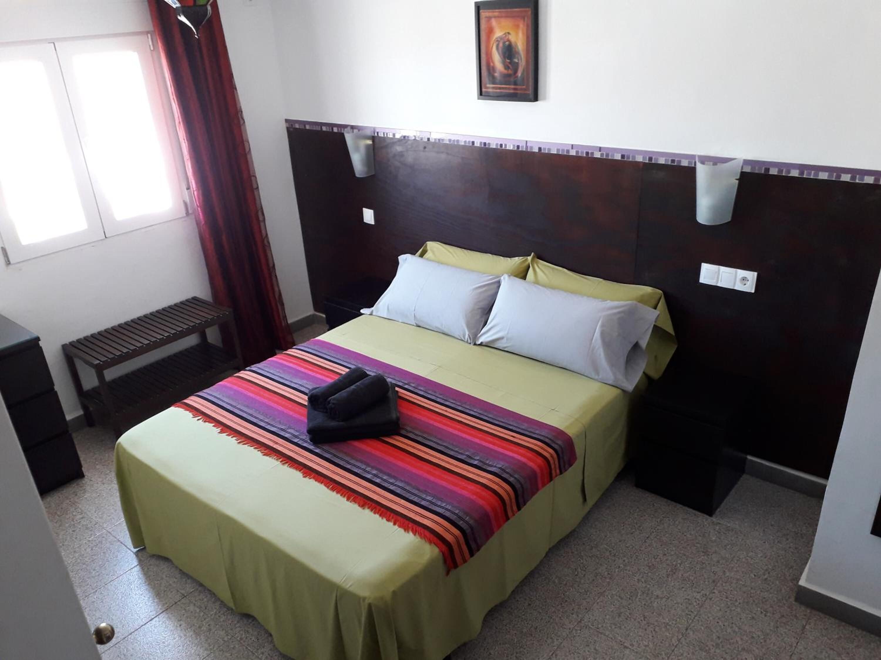 A hotel room with a bed, a bench, a window, and a painting on the wall.
