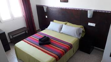 A hotel room with a bed, a bench, a window, and a painting on the wall.