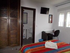 A bedroom with a bed, a desk, a chair, a TV, and a bathroom visible through an open door.