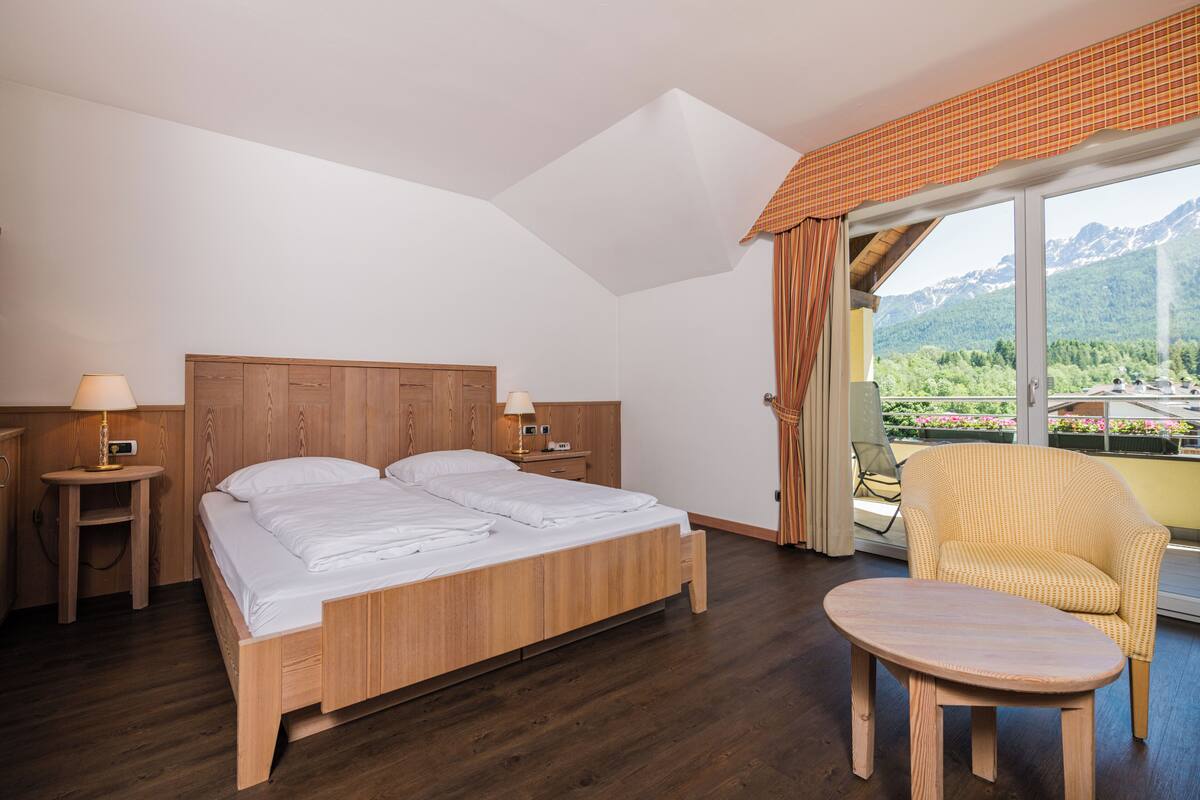 A bedroom with a wooden bed, bedside tables, a chair, and a balcony with a mountain view.