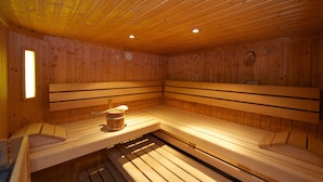 A sauna with wooden benches and a bench seat, a wooden wall, and a clock. - Pension Alpenrose (Zell am See)