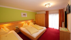 A hotel room with two beds, a wooden headboard, a red carpet, a television, and a window with curtains. - Pension Alpenrose (Zell am See)