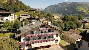 A multi-story building with balconies adorned with flowers, set in a mountainous village with houses and greenery. - Pension Alpenrose (Zell am See)