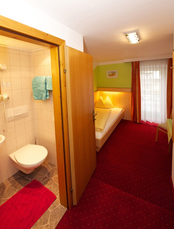 Una habitación de hotel con baño, una cama, una alfombra roja y una puerta de madera.