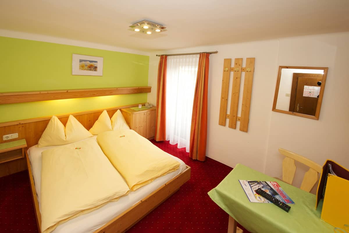 A hotel room with a bed, a desk, a chair, a mirror, and a window with curtains.