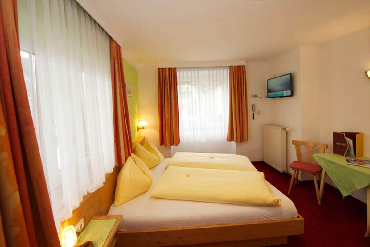 A hotel room with two single beds, a television on the wall, a desk with a chair, and a window with curtains.