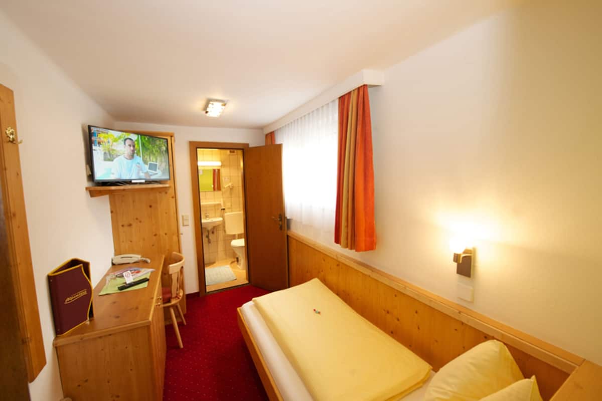 A hotel room with a bed, a desk with a telephone, a television mounted on the wall, and a bathroom visible through an open door.