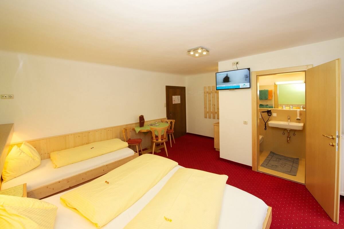 A hotel room with a bed, a desk, a TV, a bathroom, and a red carpet.