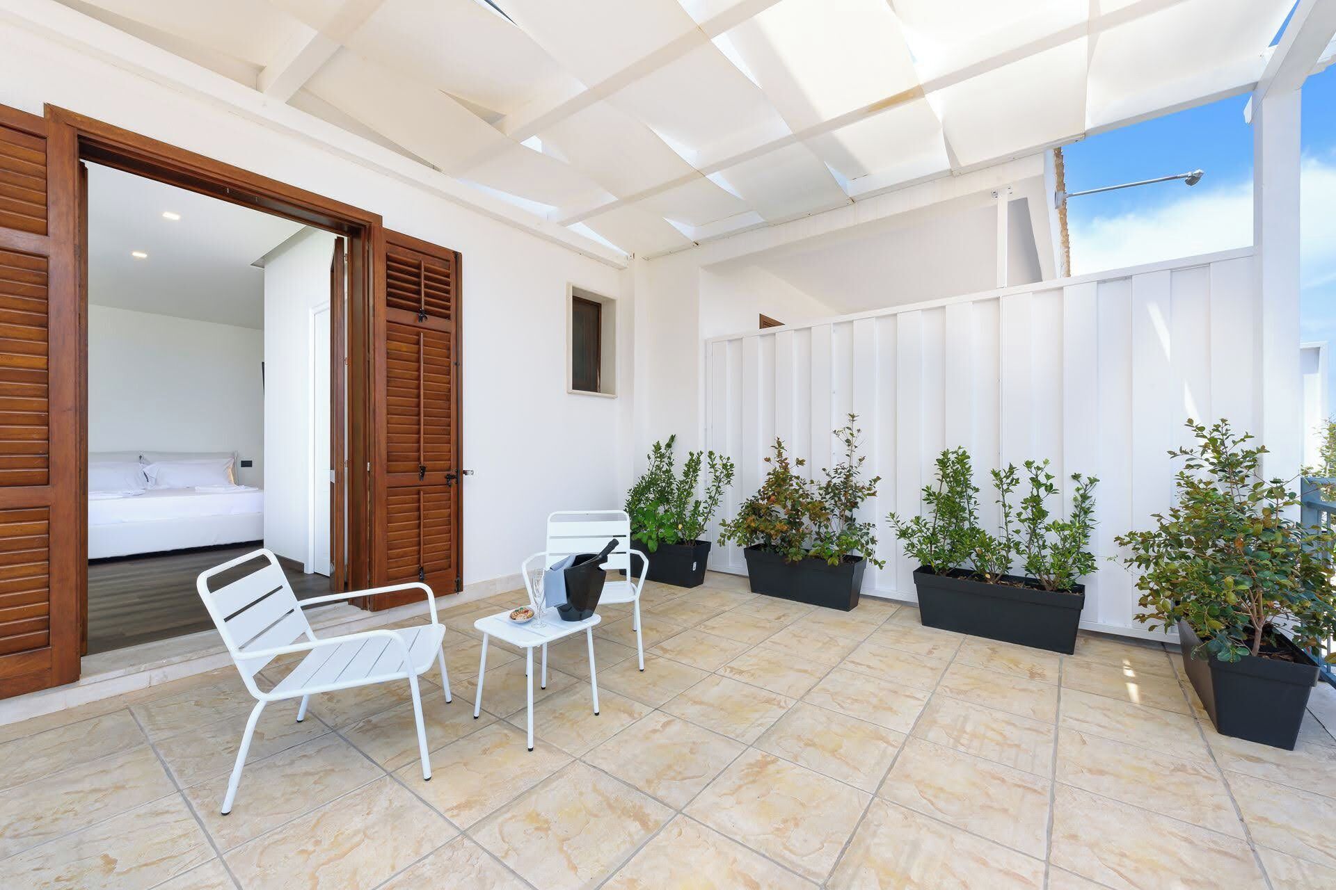A spacious patio with a white ceiling, a bed in the background, and several potted plants.