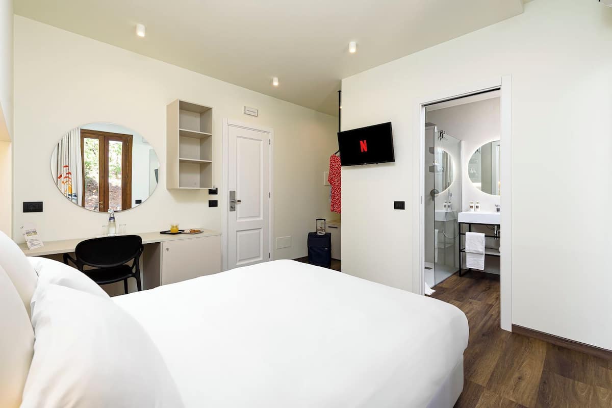 A hotel room with a bed, a desk, a TV, a bathroom, and a wardrobe.